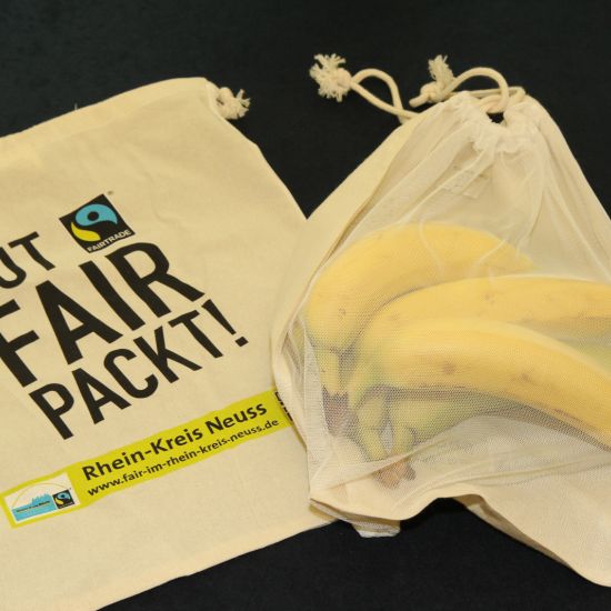 Ein Jute-Beutel mit dem Aufdruck 'Gut. Fairtrade packt an.' und ein Obstnetz mit Bananen
