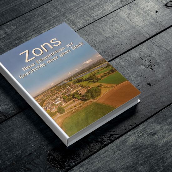 Ein geschlossenes Buch auf einem Tisch, mit einem einfachen Cover-Design. Der Titel "Zons. Neue Erkenntnisse über die Geschichte einer alten Stadt" ist deutlich sichtbar und das Buch scheint in gutem Zustand zu sein, bereit zum Lesen oder zur Aufbewahrung in einer Bibliothek.