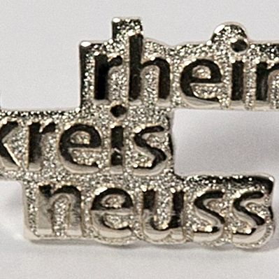 Ein silberfarbener Ansteck-Pin mit dem Schriftzug "rhein kreis neuss" 